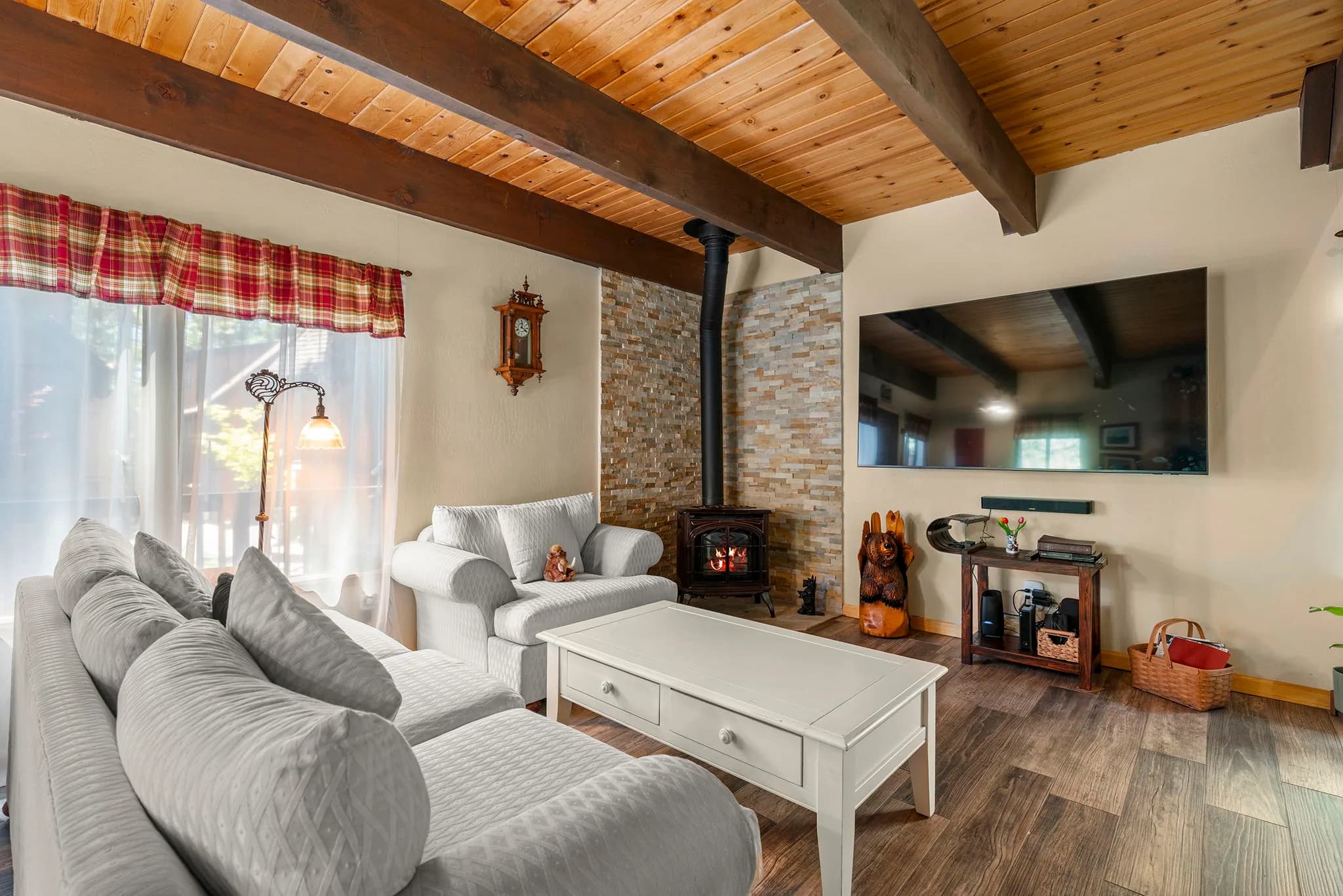Living room with exposed wood ceiling, large windows, and a freestanding gas stove